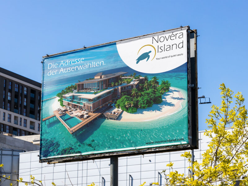 Maria_Enzinger_Referenzbild-Novera-Island-Plakat Plakatwand mit Banner von "Novéra Island. Im Hintergrund sieht man ein Haus, eine Mauer und einen Strauch.